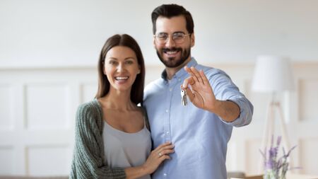 Portrait of happy millennial couple hug look at camera smile showing house keys moving in together, excited young husband and wife feel overjoyed relocating to new home, ownership conceptの写真素材