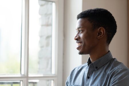 Smiling African American businessman looking at window and thinking about good future close up, motivated employee executive dreaming, pondering project strategy or startup idea, business visionの写真素材