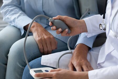 Close up doctor cardiologist wearing white uniform checking older woman blood pressure with digital...