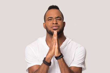 Hopeful african American man in glasses join hands in prayer hope for best, superstitious black...