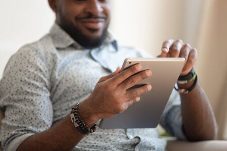 Close up focus african male hands holds tablet, guy sitting indoors with electronic device modern wireless gadget, spend free time chat online, browse websites, freelancer working in internet conceptの写真素材
