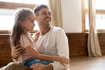 Happy loving young dad sit on warm home wooden floor playing with little preschooler cute daughter, smiling Caucasian father cuddle have fun enjoy family weekend together with small girl childの写真素材
