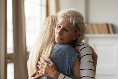 Young empathic woman embracing soothing comforting frustrated older mature mother. Grownup daughter apologizing to offended middle aged mommy. Two female generations family overcoming grief together.の写真素材