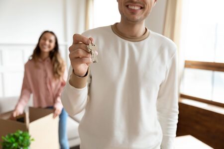 Smiling young man show house keys excited to move together with overjoyed beautiful millennial wife,...