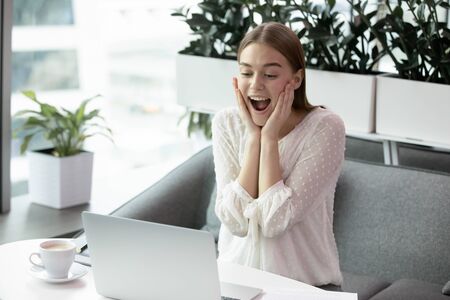 Excited young woman feeling amazed, looking at computer screen, working in modern office alone. Happy millennial girl surprised by email with good news, university admission, dream job hiring.の写真素材