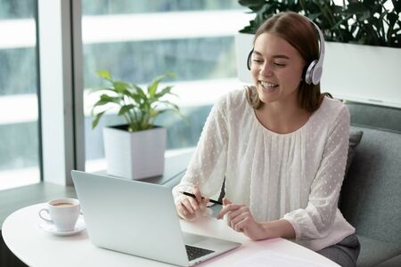 Happy young employee wearing wireless headphones, holding video call with client. Excited millennial...