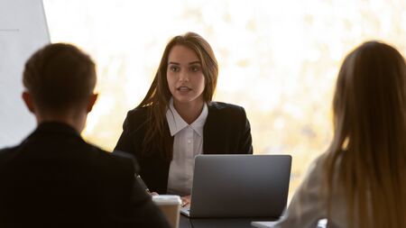 Businesspeople negotiating sit at desk in boardroom, focus on young confident business lady express opinion talking with partners take part at group meeting solving current issues, cooperation conceptの写真素材