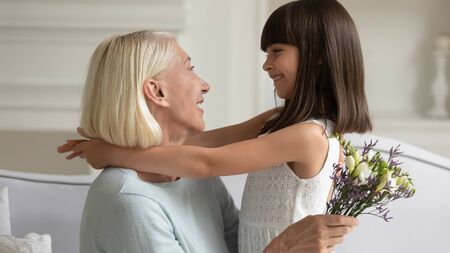 Happy little preschooler girl hug smiling senior grandmother greeting her with anniversary...