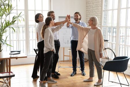 Overjoyed diverse business people stand give high five join hands celebrate shared business victory in office, happy smiling colleagues engaged in teambuilding activity at meeting, teamwork conceptの写真素材