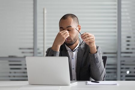 Tired businessman take off glasses feel fatigue suffering from headache or dizziness overwork at laptop, exhausted male employee take break from work massaging eyes having blurry visionの素材 [FY310140249344]