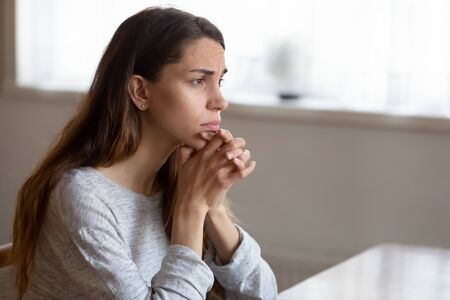 Sad pensive young woman look in distance feel stressed thinking of life relationships problems, thoughtful unhappy millennial girl lost in thoughts mourn, suffer from depression or mental disorderの写真素材