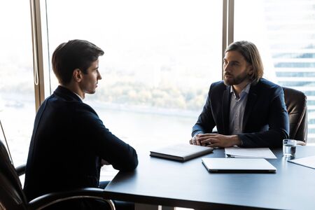 Serious businessman talking with mentor coach lead in office at meeting. Young employee discussing...