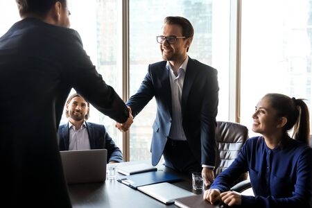 Happy successful businessman in suit shaking hand of applicant at interview. HR manager making good first impression. Employer congratulates attractive happy male candidate getting hired.の写真素材