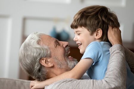 Side view head shot close up overjoyed older mature granddad embracing little grandson. Happy excited middle aged man having fun with laughing little boy, different generations relations concept.の写真素材
