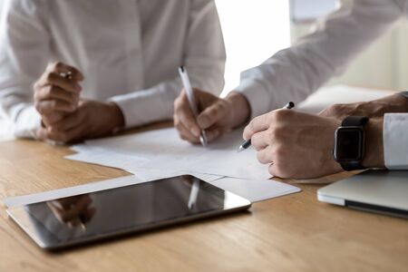 Diverse business partners working sitting at office desk close up view hands documents at tablet...
