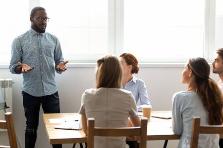 African American coach holding briefing with employees in boardroom, making presentation, explaining business strategy or startup, staff training concept, colleagues discussing project at meetingの写真素材