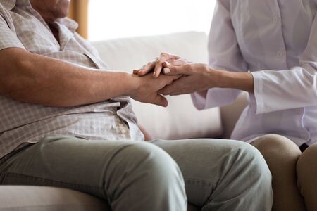 Close up of supportive female doctor hold senior male patient hands show care and understanding, woman nurse or medical worker comfort worried mature man client, elderly healthcare conceptの写真素材