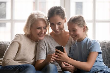 Happy three generations middle aged retired grandmother, smiling young mother and girl sitting...