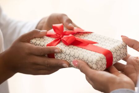 African american child kid hands holding gift box red ribbon give christmas present to mom congratulating with happy birthday mothers day concept, making surprise on holiday background, close up viewの写真素材