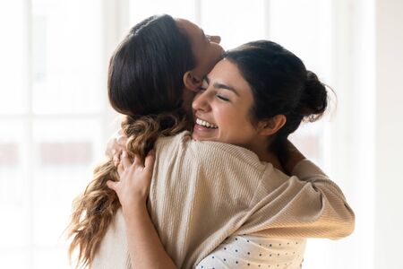 Candid diverse girls best friends embracing standing indoors, close up satisfied women face enjoy tender moment missed glad to see each other after long separation, friendship warm relations conceptの写真素材