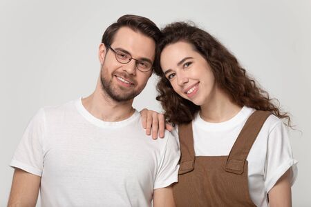 Head shot close up portrait young romantic bonding family couple looking at camera. Happy millennial girl puts hand on boyfriends shoulder, standing head to head isolated on grey studio background.の写真素材