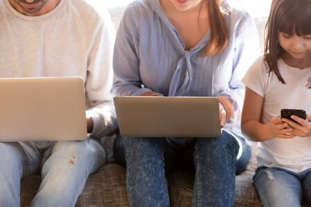 Close up of young family with preschooler kid sit on couch busy using electronic devices, modern parents and little daughter addicted to gadgets, lack real communication. Technology conceptの写真素材