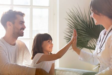 Smiling preschooler girl with young dad give high five to visiting doctor or nurse, happy father...