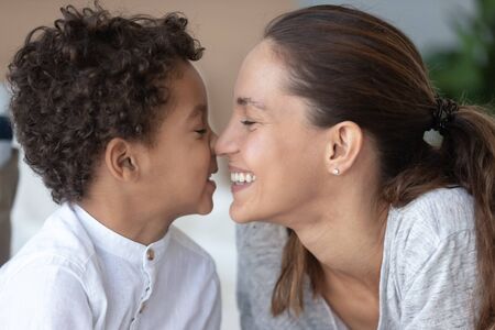Loving mother and African American little son touching noses close up, expressing love, smiling mom and adorable child enjoying funny moment, free time together, playing, family having funの写真素材