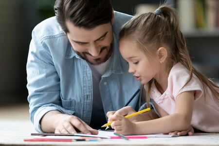 Caring young father lying on floor drawing with colorful pencils with little daughter, loving dad...