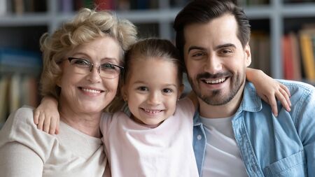 Portrait of smiling senior grandmother posing with grown-up son and little preschooler granddaughter...