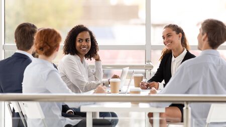 Young smiling diverse women in boardroom at meeting. Happy black and white business partners...