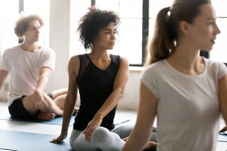 African ethnicity woman with group of diverse people seated in lotus pose practicing yoga asanas...