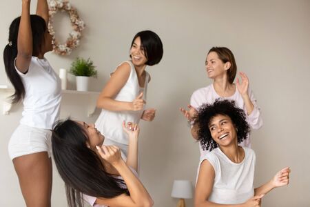 Pretty African American girl wearing pajamas dancing to favorite with friends at sleepover or...