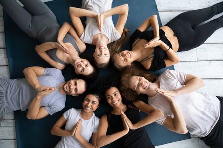 Above view seven multi ethnic people in sportswear lying down on mats in circle folded palms together showing Namaste gesture symbol of salutation, express gratitude for gained knowledge at yoga classの写真素材