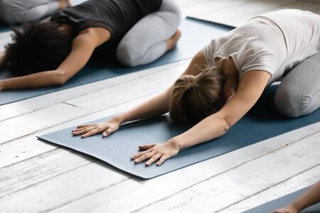 Young women practicing asana lying down on mats at therapy session close up focus on Caucasian girl performing Child Pose reduce fatigue after workout, posture relief of stress. Yoga activity conceptの写真素材