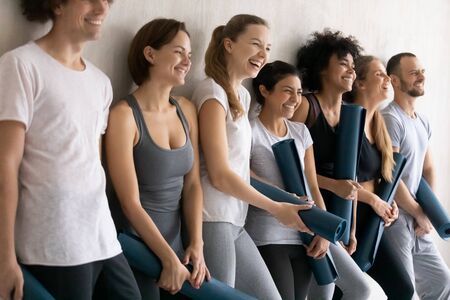 Sportive diverse people wearing comfy stylish sportswear holding yoga mats leaned on wall ready for training at gym. Wellness, sport club studio staff portrait, seminar, team building activity conceptの写真素材