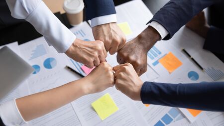 Close up top view of diverse multiethnic businesspeople give fists bump engaged in teambuilding...