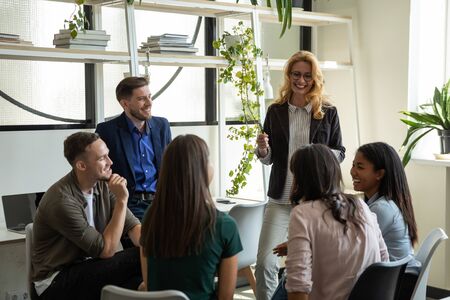 Smiling middle-aged Caucasian businesswoman talk lead meeting with multiracial diverse colleagues in office, female boss speak with multiethnic coworkers, brainstorm with employees at briefingの写真素材