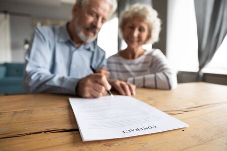 Close up of happy mature 60s couple spouses clients close deal sign insurance contract with specialist, smiling middle-aged old husband and wife put signature make agreement, elderly care conceptの写真素材