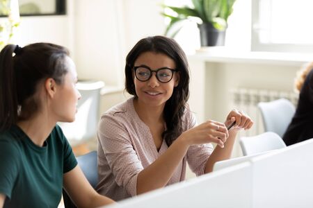 Diverse millennial female employees talk discuss business ideas collaborating using computer in...