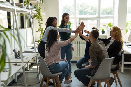 Excited multiracial colleagues give high five celebrate company business success at briefing,...