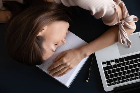 Top above view head shot close up restless young woman freelancer sleeping on table, tired of hard...