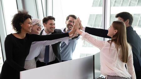 Overjoyed multiracial businesspeople give high five engaged in teambuilding activity or training at...