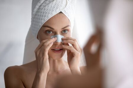 Focused young beautiful woman with towel on head applying cleaning strip, removing dark spots....