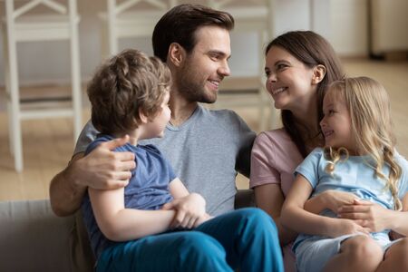 Close up of happy young parents with two small children sit on couch relax enjoy family weekend at home together, smiling mom and dad rest with kids on comfortable sofa in new own apartmentの写真素材