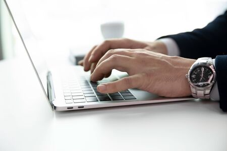 Close up of successful businessman sit at desk work on modern laptop gadget typing texting on...
