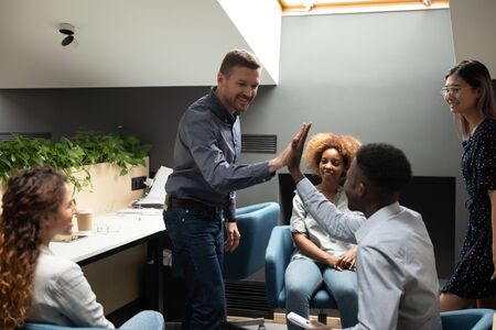 Smiling team leader giving high five to African American employee at briefing, executive thanking...