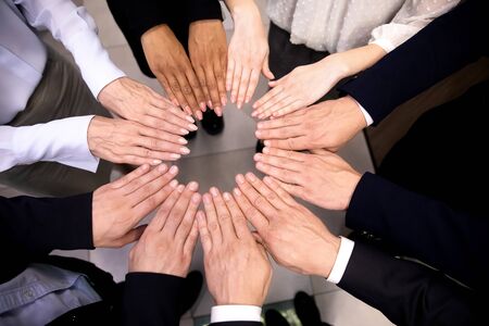 Close up top view of multiracial colleagues join hands in circle show unity and support at work,...