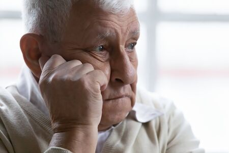 Old man feeling disappointed, lost in sad thoughts close up portrait. Baby boomer generation 80s grandfather suffers from loneliness, chronic or dementia senile diseases, life troubles regrets conceptの写真素材
