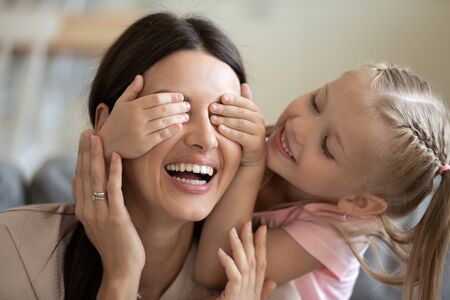 Close up of cute little girl close smiling mother eyes have fun involved in funny activity at home, overjoyed small preschooler daughter play with happy young mom enjoy playful weekend time togetherの写真素材